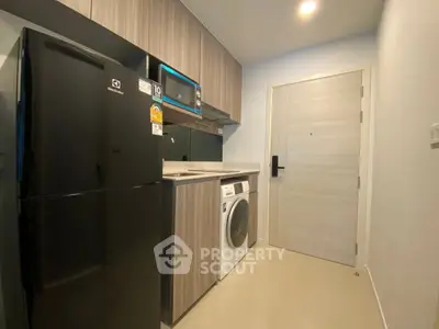 Modern compact kitchen with fridge, microwave, and washing machine in sleek apartment.