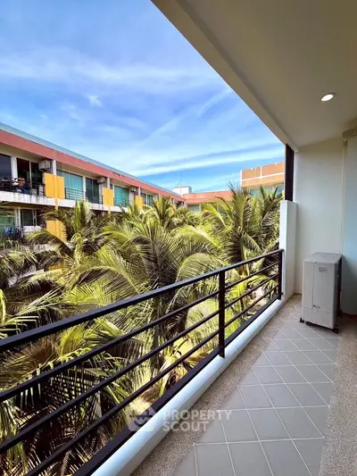Spacious balcony with lush palm tree views in modern apartment complex.