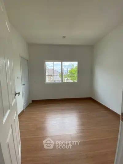 Spacious empty room with wooden flooring and large window offering natural light.