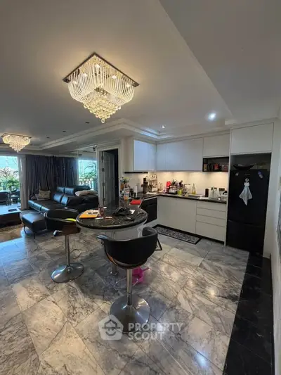 Luxurious open-layout kitchen and living room with elegant chandeliers and marble flooring.