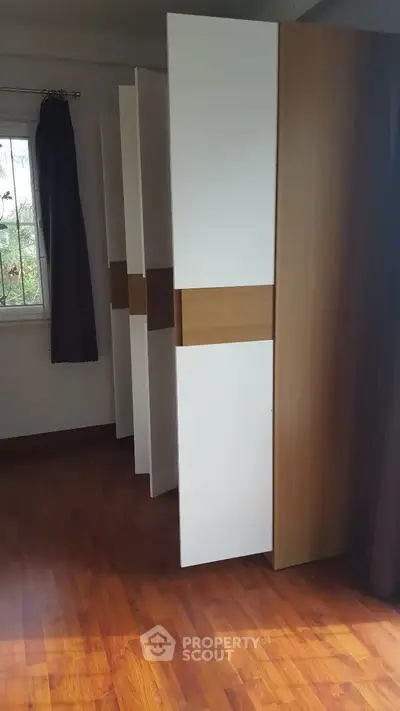 Spacious bedroom with modern wooden flooring and large window for natural light.