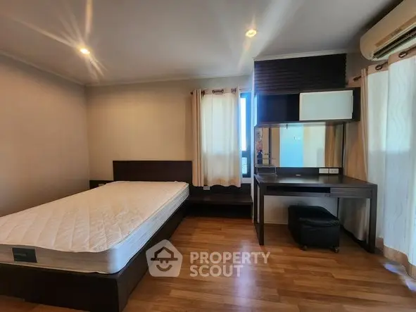 Spacious bedroom with wooden flooring and modern furniture in a well-lit apartment.