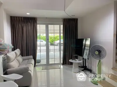 Cozy living room with modern sofa and large TV, bright natural light from glass doors