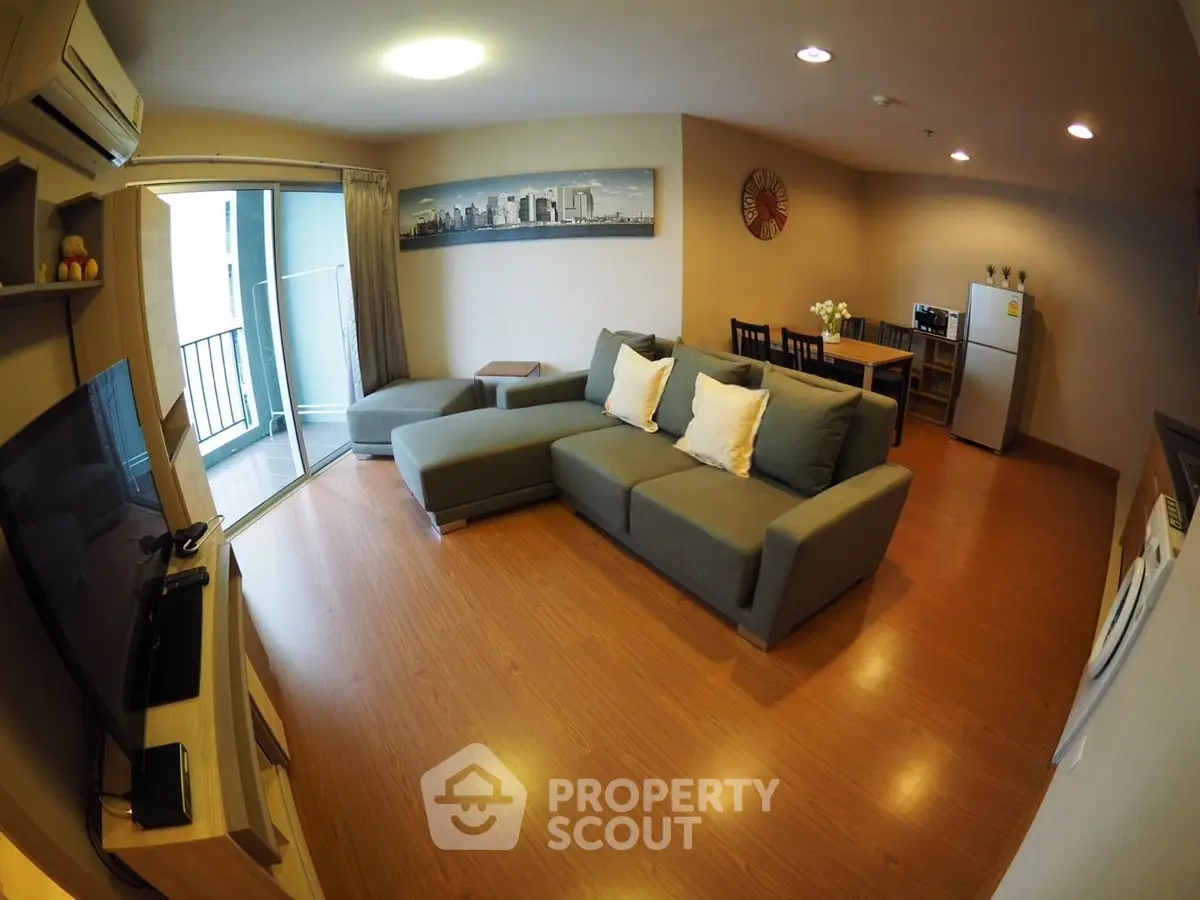 Spacious modern living room with open layout and balcony access, featuring stylish furniture and wooden flooring.