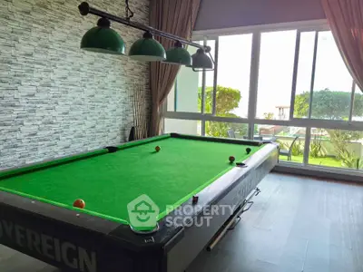 Spacious game room with pool table and large windows overlooking garden view.