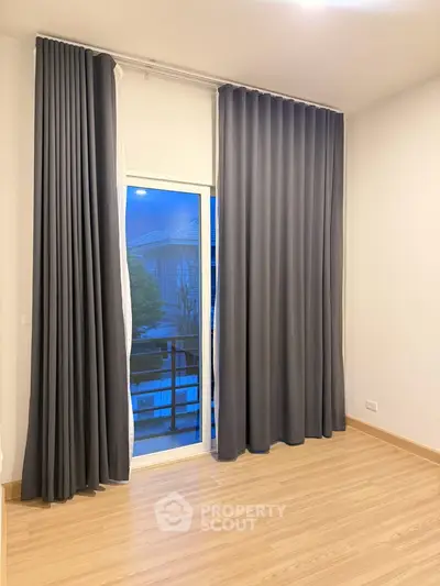 Spacious room with large window and elegant curtains, offering a serene view.