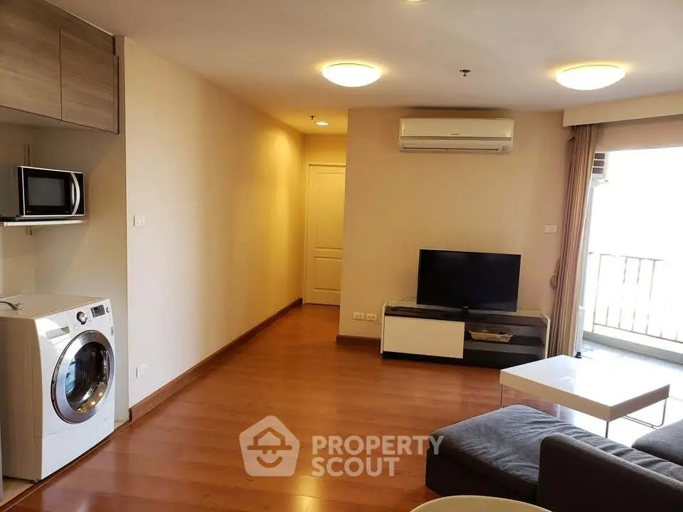 Modern living room with wooden flooring, washing machine, and balcony access in a stylish apartment.