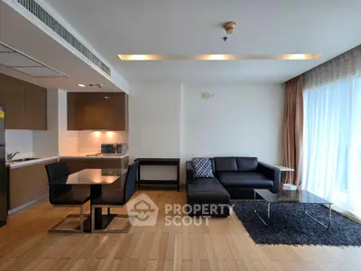 Modern living room with sleek furniture and open kitchen layout, featuring natural light and stylish decor.