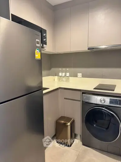 Modern kitchen with sleek appliances, featuring a fridge and washing machine in a compact layout.