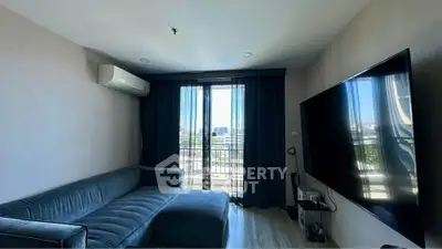 Modern living room with large TV and balcony view, featuring sleek furniture and natural light.