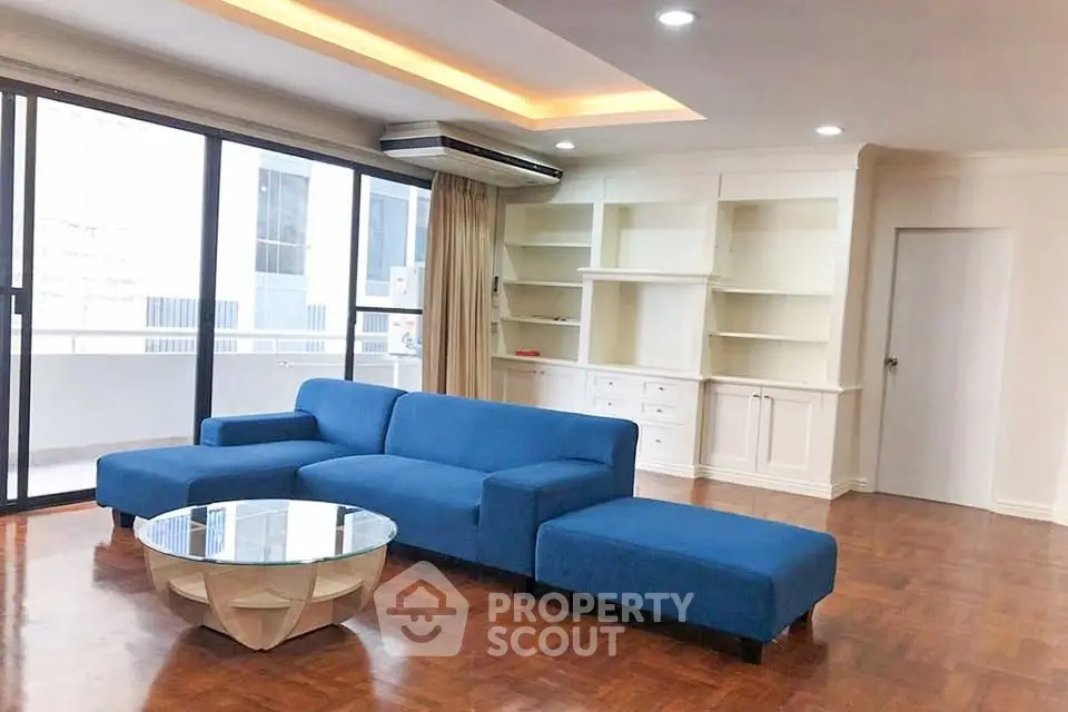 Spacious living room with modern blue sofa and large windows leading to a balcony.