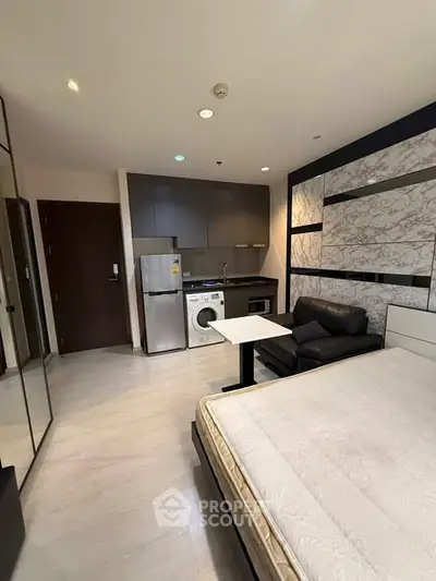 Modern studio apartment with sleek kitchen and cozy living area, featuring a washing machine and stylish decor.