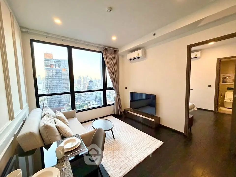 Modern living room with city view, featuring sleek furniture and large windows in a high-rise apartment.