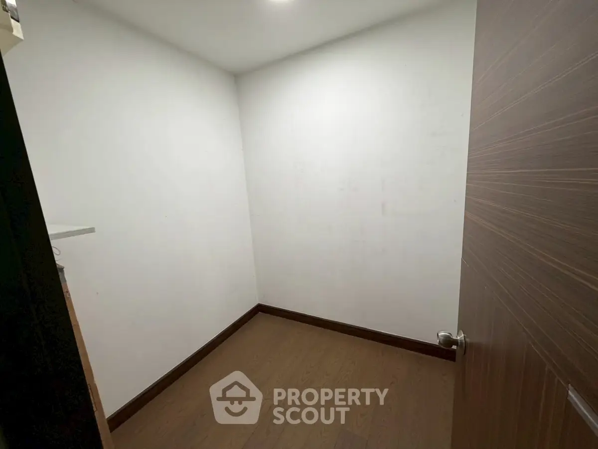 Compact storage room with wooden flooring and white walls, ideal for organizing essentials.