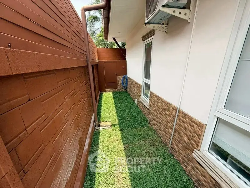 Narrow side yard with grass and brick wall, adjacent to a house exterior.