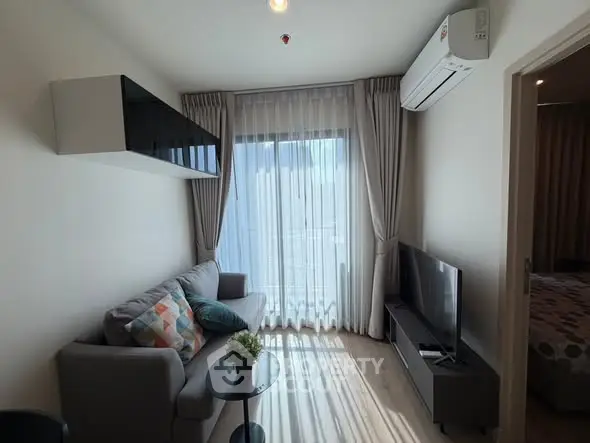 Modern living room with cozy sofa, TV, and large window with sheer curtains.