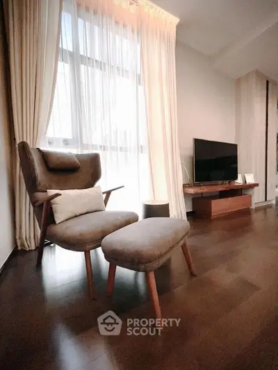 Elegant living room with cozy armchair, ottoman, and modern TV setup, featuring warm lighting and stylish decor.