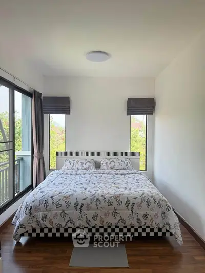 Cozy bedroom with large windows and stylish decor, offering a serene view and ample natural light.