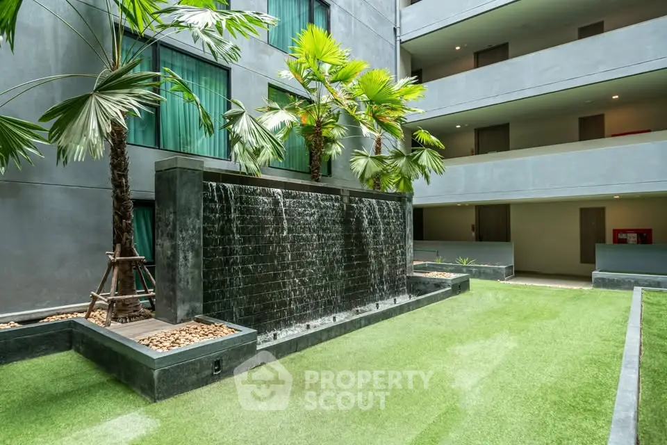 Modern apartment building with lush courtyard and waterfall feature, offering serene living environment.