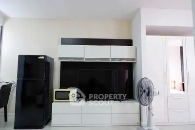 Modern living room with sleek furniture and appliances, featuring a black fridge and flat-screen TV.
