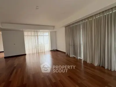 Spacious empty living room with wooden floors and large windows with curtains.