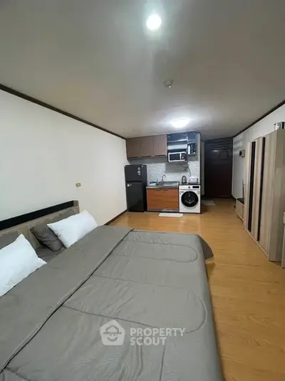 Modern studio apartment with integrated kitchen and cozy sleeping area, featuring wooden flooring and sleek appliances.