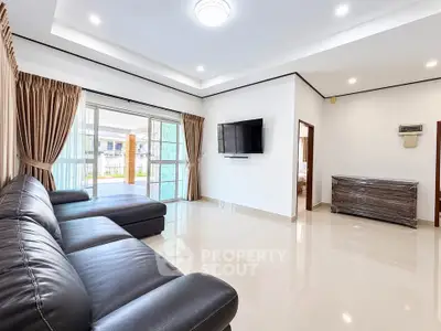 Spacious modern living room with leather sofa and wall-mounted TV, featuring large windows and elegant curtains.