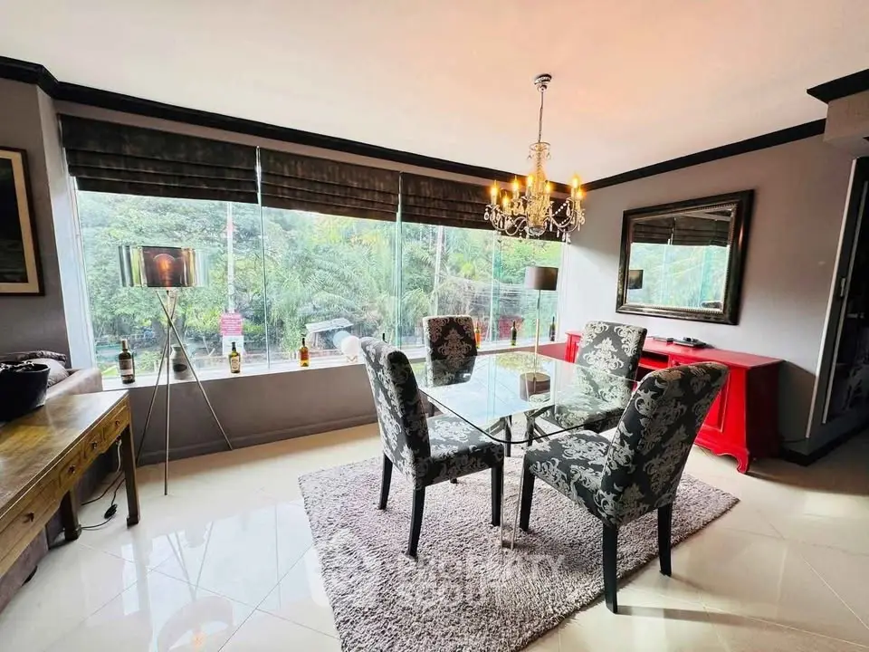 Elegant dining room with glass table, plush chairs, and chandelier overlooking lush greenery.