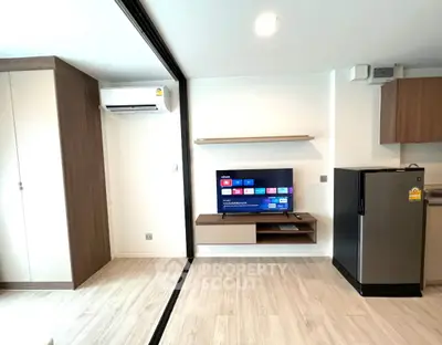 Modern living room with sleek TV setup and compact kitchen area in stylish apartment.