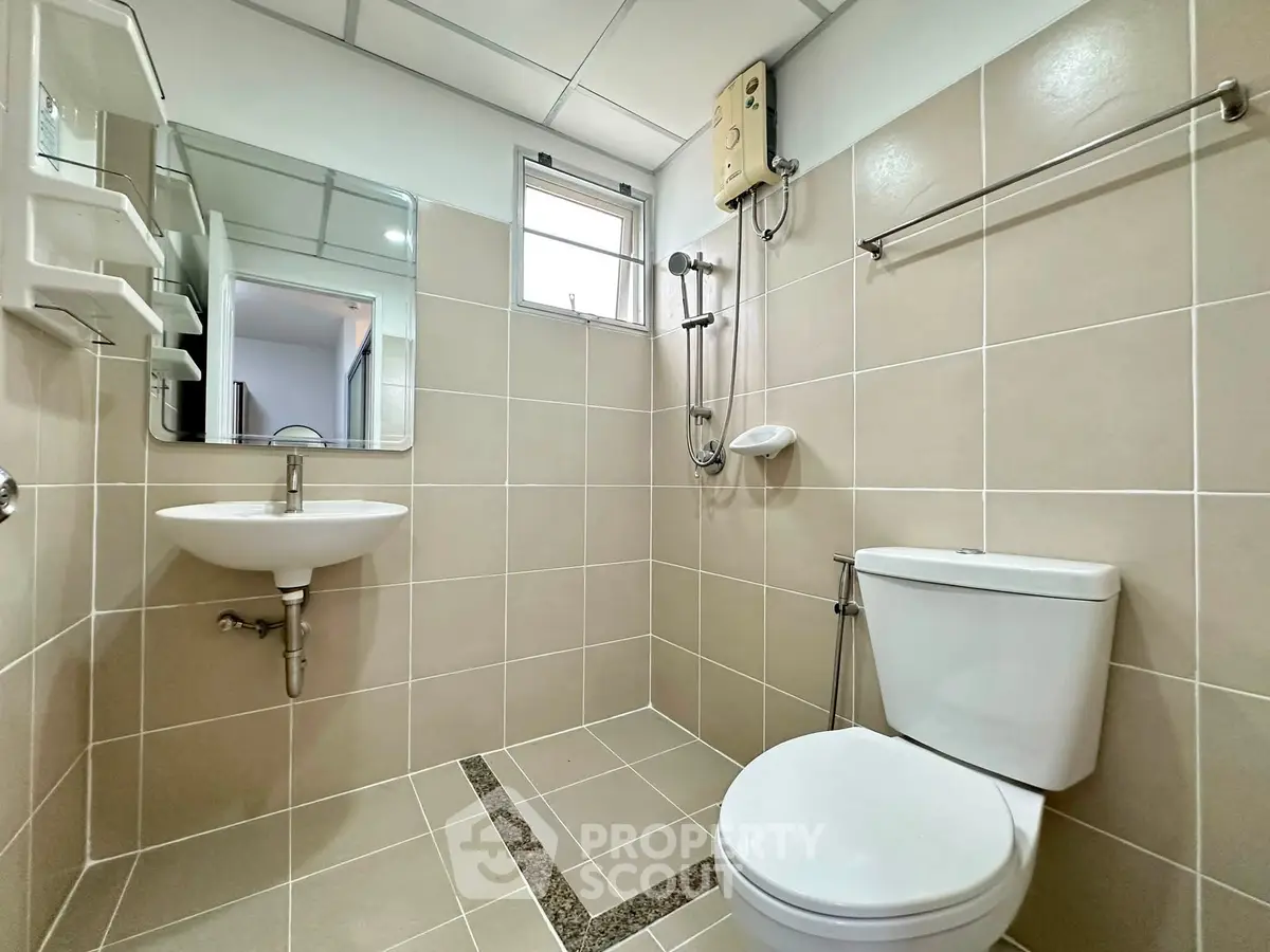 Modern bathroom with sleek fixtures and neutral tiles, featuring a shower and toilet in a compact layout.