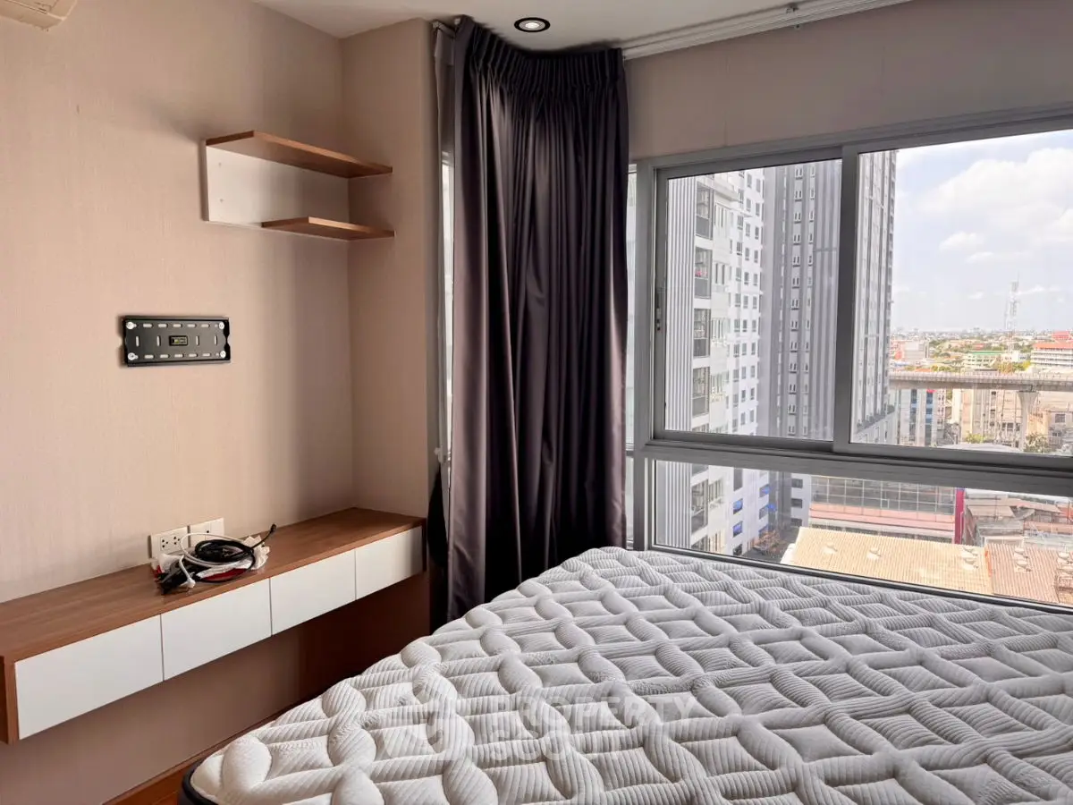 Modern bedroom with large window offering city view, featuring a comfortable mattress and sleek wooden shelves.