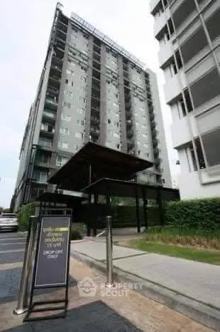 Modern high-rise building exterior with sleek entrance and lush greenery.
