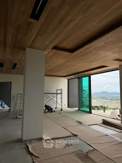 Spacious modern living room under construction with panoramic windows and wooden ceiling.