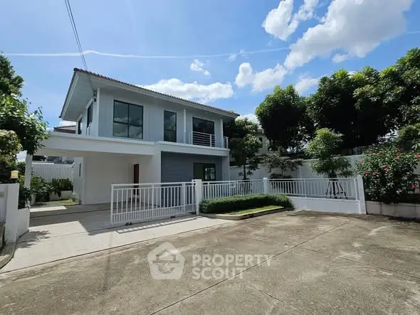 Modern two-story house with spacious driveway and lush greenery under a clear blue sky.