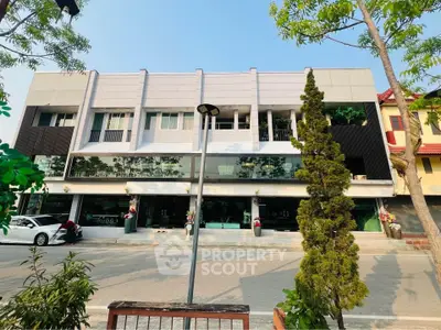 Modern commercial building exterior with large glass windows and trees lining the street.