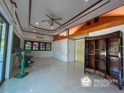 Spacious living room with high ceiling, tiled floors, and wooden accents, featuring a ceiling fan and large windows for ample natural light.