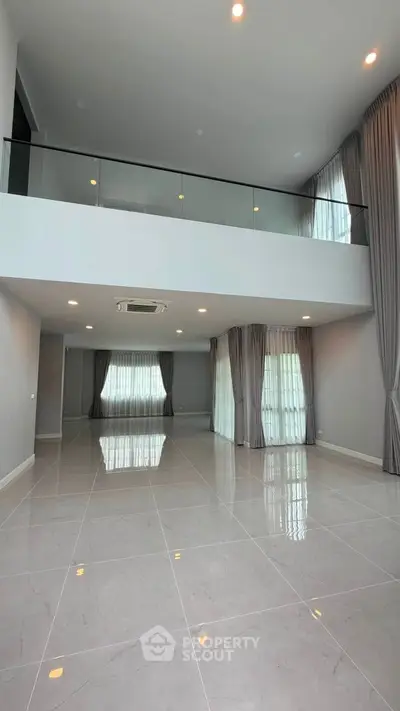 Spacious modern living room with high ceilings and large windows, featuring elegant curtains and sleek tile flooring.