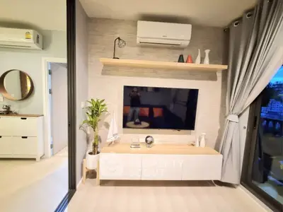 Modern living room with stylish decor and large TV, featuring air conditioning and natural light.