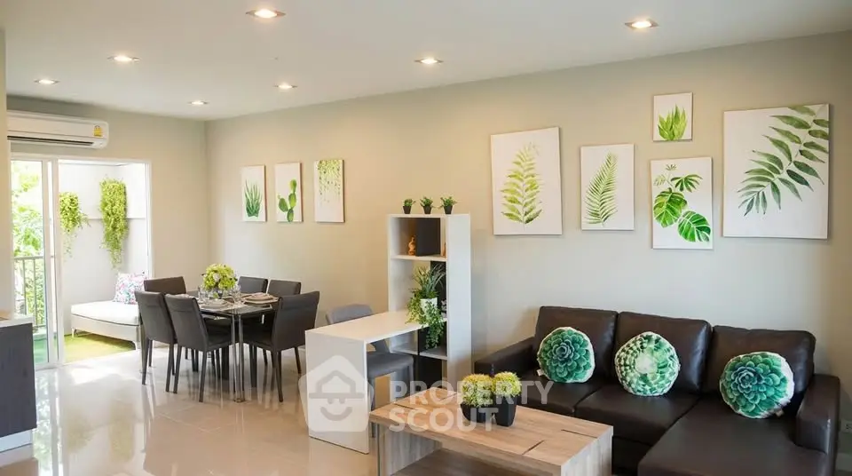 Modern living room with stylish decor and open dining area, featuring lush green accents and natural light.