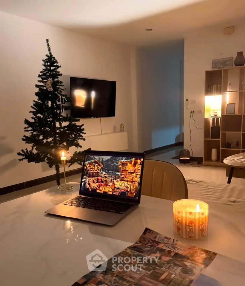 Cozy living room with holiday decor, featuring a lit candle, laptop, and a small Christmas tree.