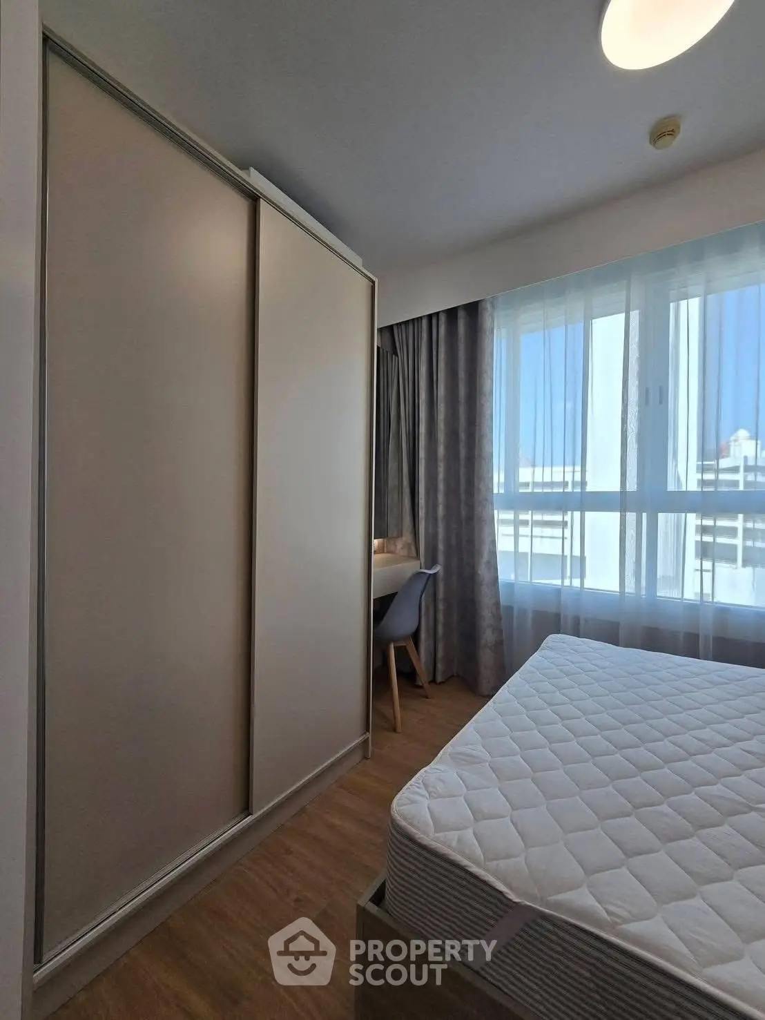 Modern bedroom with large window and built-in wardrobe, offering ample natural light and cozy ambiance.