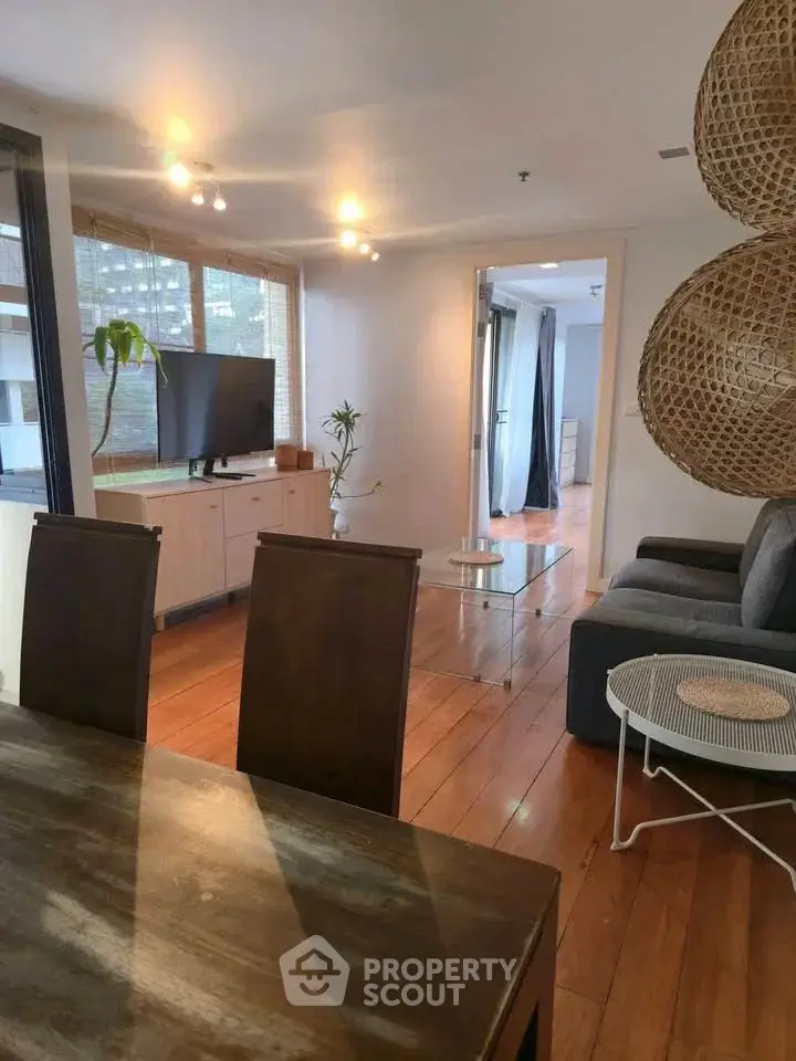 Spacious living room with modern decor and wooden flooring, featuring a cozy seating area and large windows.