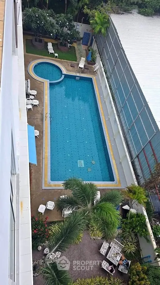 Stunning aerial view of a luxurious swimming pool with lush greenery and seating area, perfect for relaxation.