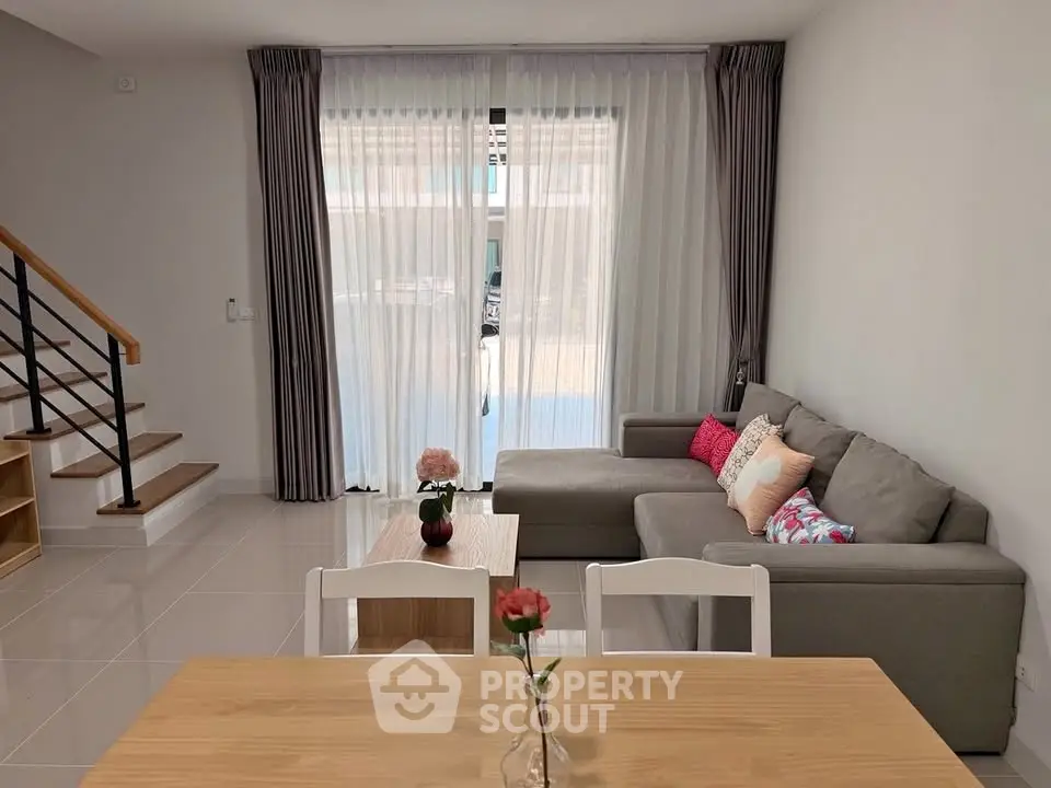 Modern living room with cozy gray sofa, wooden staircase, and elegant curtains in a bright, inviting space.