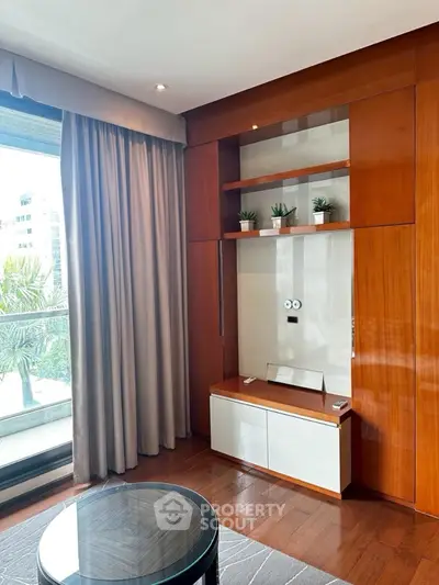 Elegant living room with wooden cabinetry and large window offering natural light and greenery view.