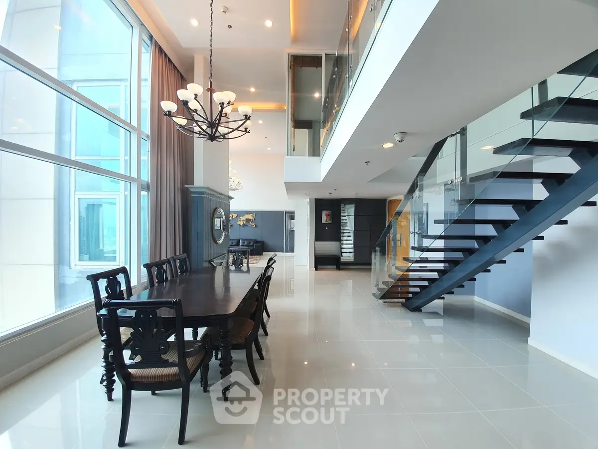 Luxurious open-plan living and dining area with high ceilings and modern staircase in a contemporary apartment.