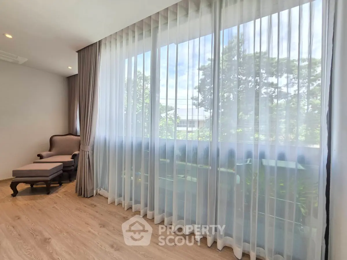 Spacious living room with large window and elegant armchair, offering serene garden views.