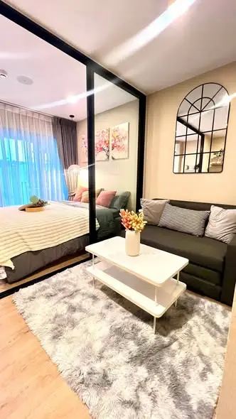 Modern studio apartment with cozy living area and stylish bedroom separated by glass partition.
