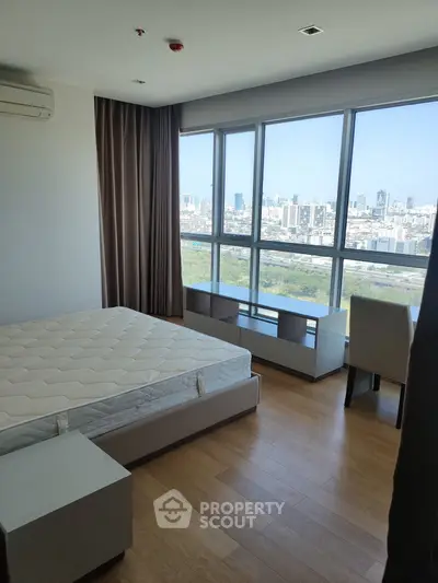 Spacious bedroom with large windows offering stunning city views, featuring modern furnishings and hardwood floors.