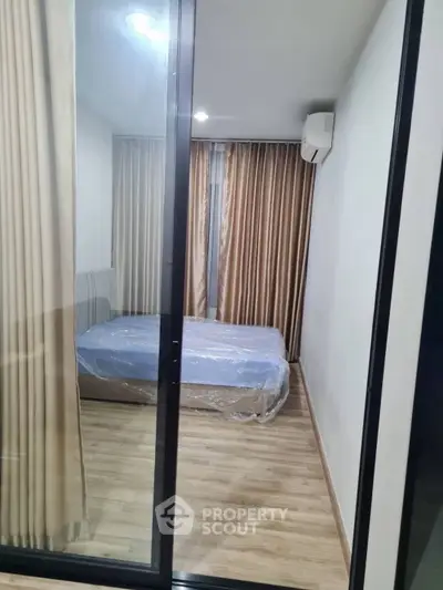 Modern bedroom with wooden flooring and large window draped with curtains.